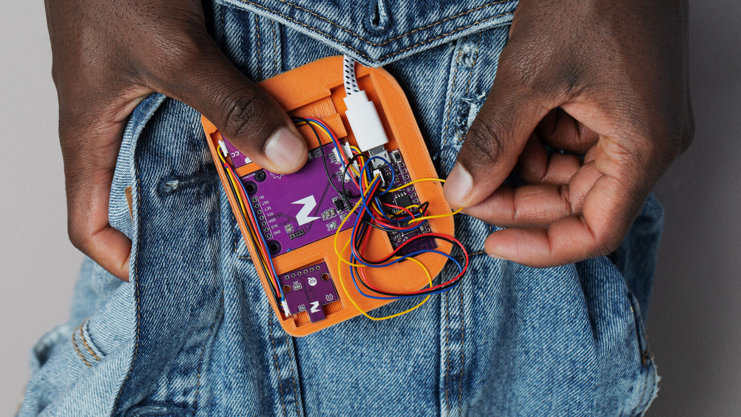 Hands holding an orange electric open device over a jeans jacket