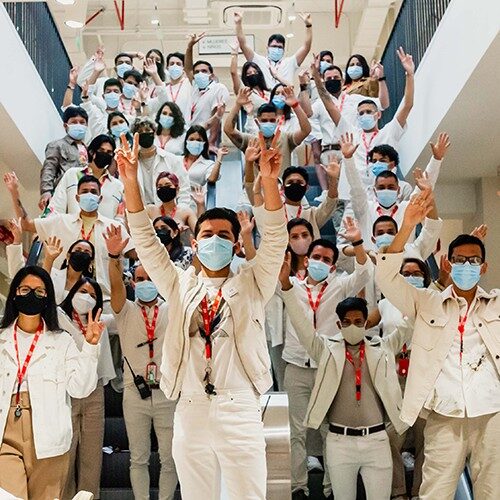 Un gran grupo de empleados de la tienda con máscaras saludando a la cámara